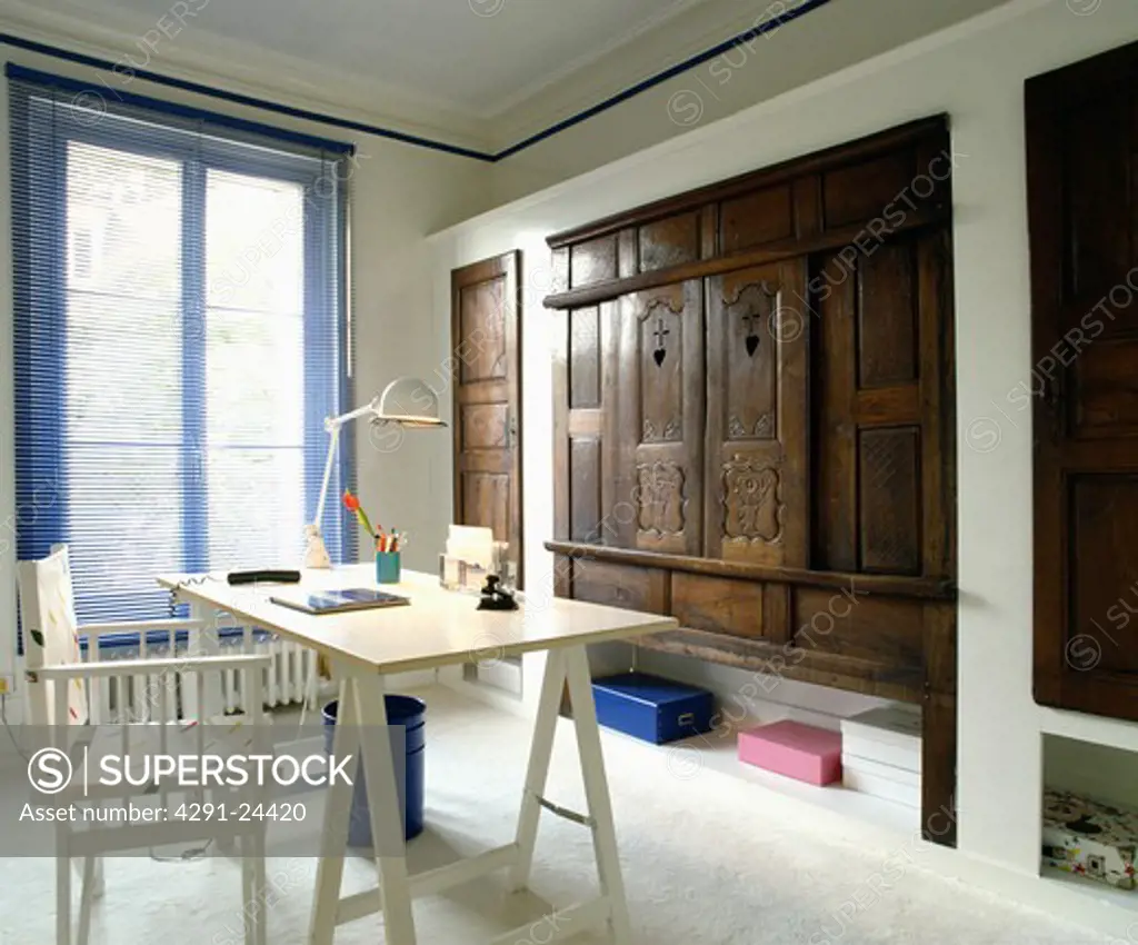 Director's chair and modern trestle table in home office with old carved wooden doors on cupboard