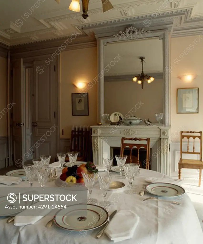 Wall-lights on either side of ornate grey mirror in traditional dining room with place settings on white tablecloth