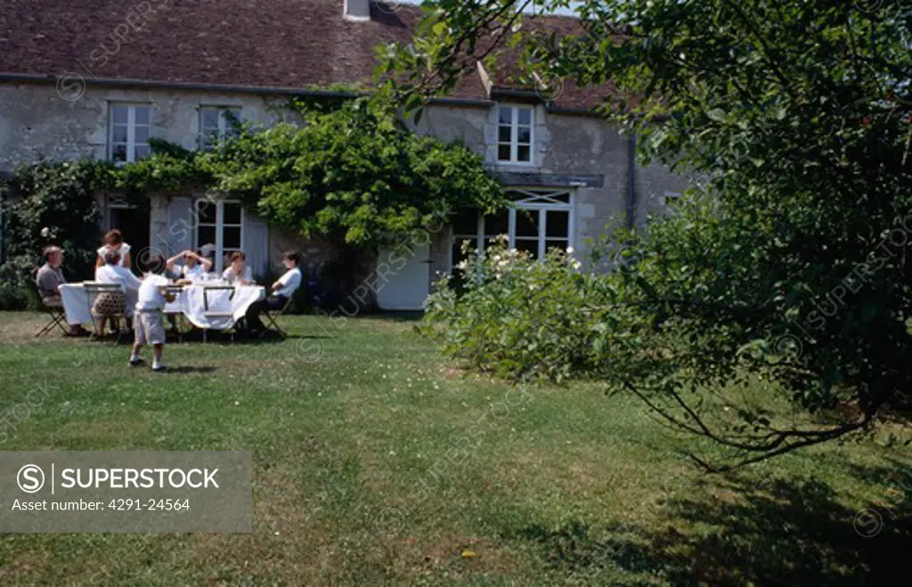 Family having tea on lawn in garden of French country house