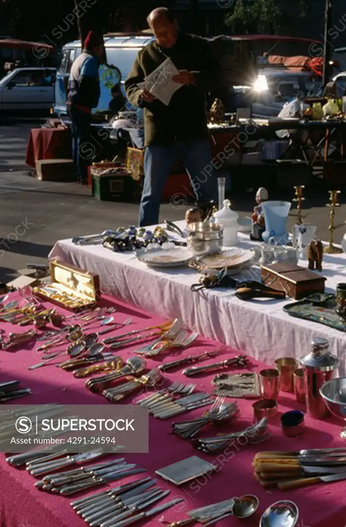 Stall-holder at street market in Paris with cutlery laid out on pink cloth on ground
