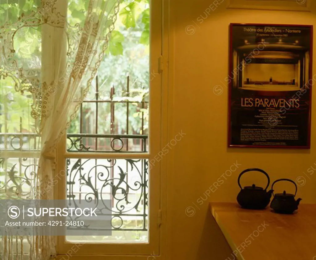 Japanese teapots below poster on wall beside French windows with white lace curtain