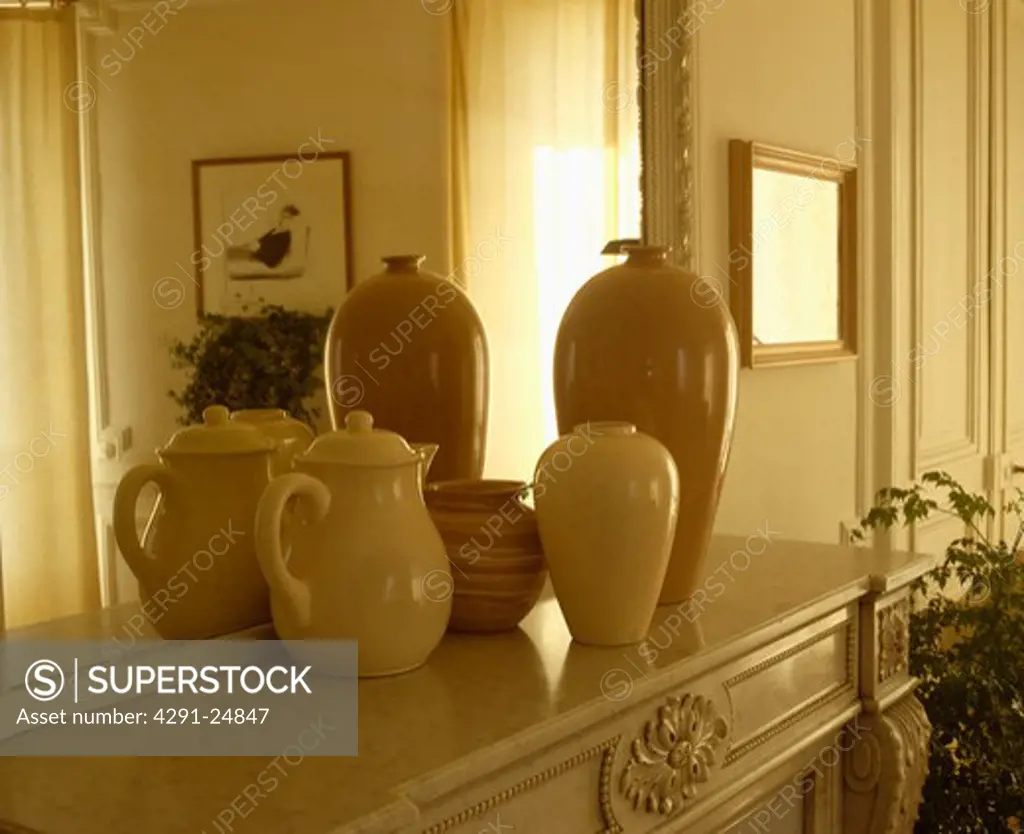 Close-up of collection of cream vases in front of mirror above mantelpiece