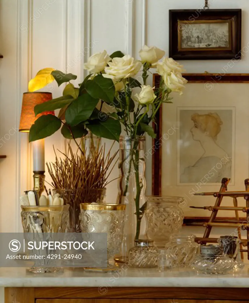Close-up of glasses and cream roses in vase on mantelpiece