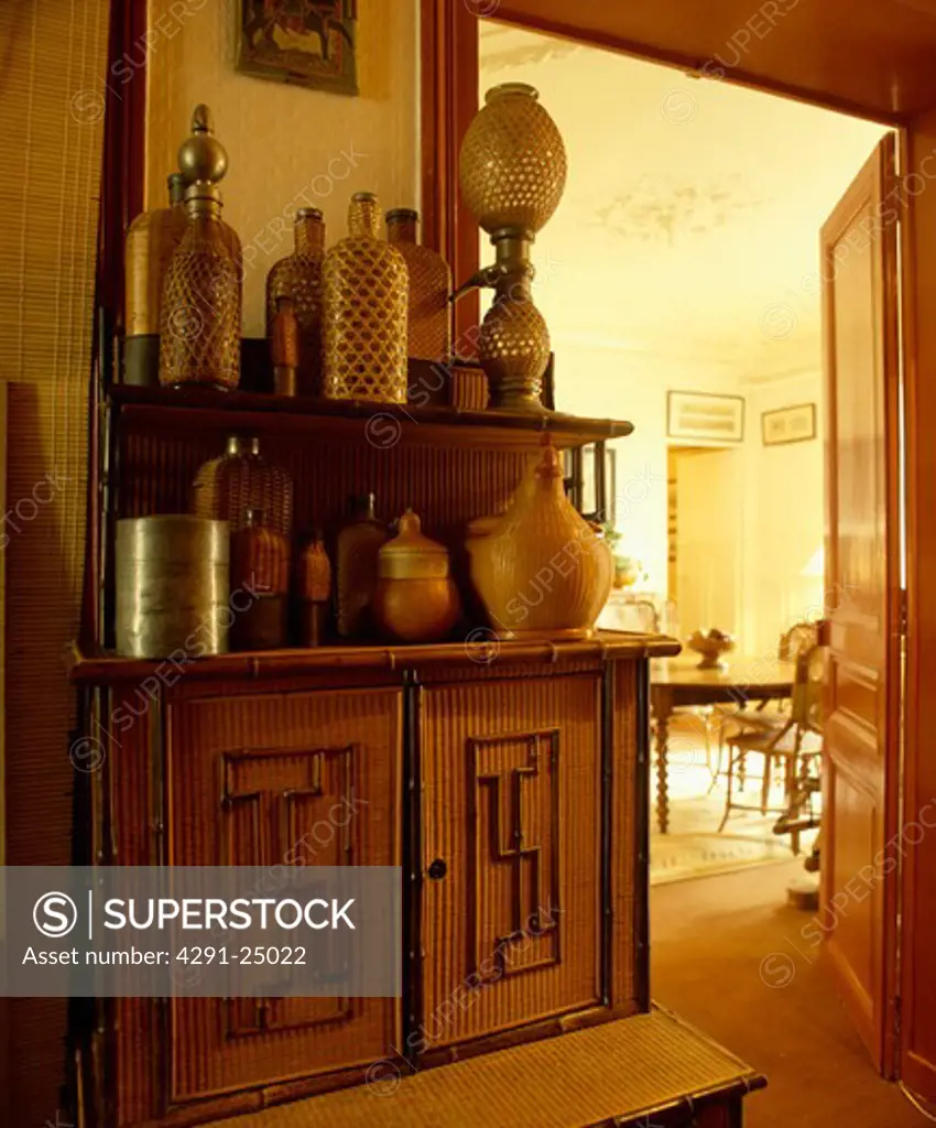 Collection of large rattan bottles on bamboo cupboard in hall beside open door to dining room