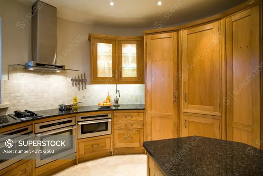 Fitted oak storage cupboards and tumbled marble mosaic wall tiles in oast house kitchen