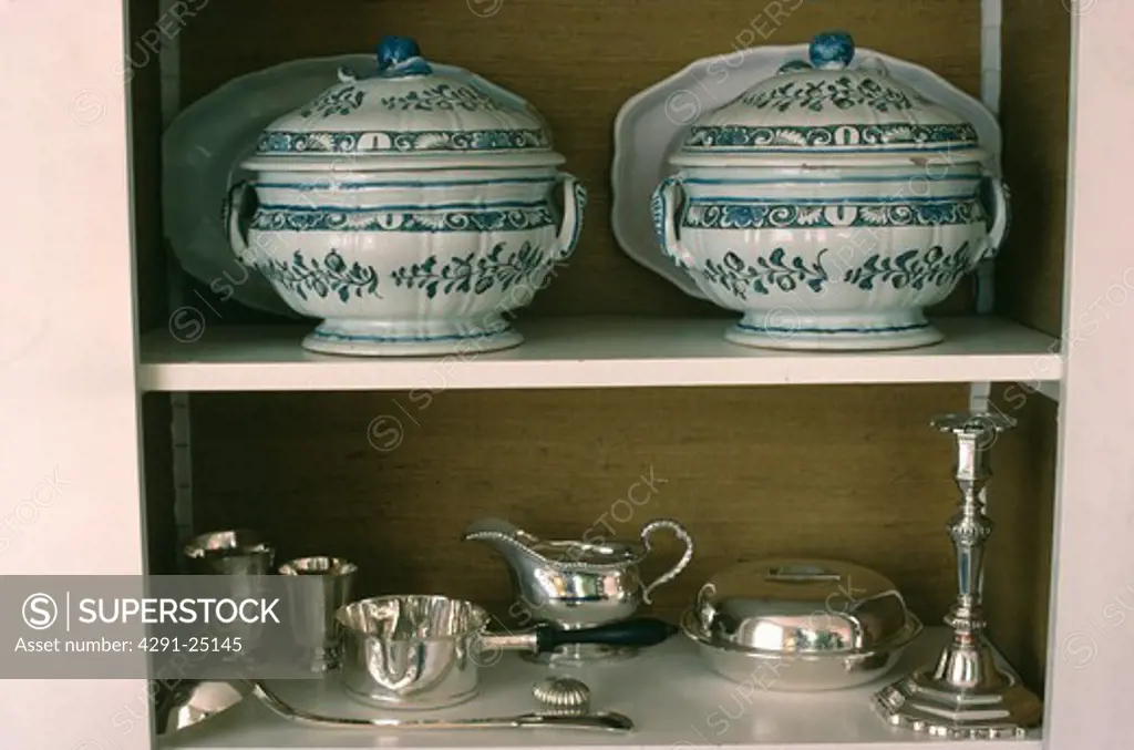 Close-up of antique tureens and silver jugs and dishes on white shelves