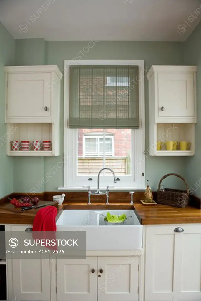Green Pinoleum blind on window above white ceramic double sink in kitchen with cream fitted cupboards