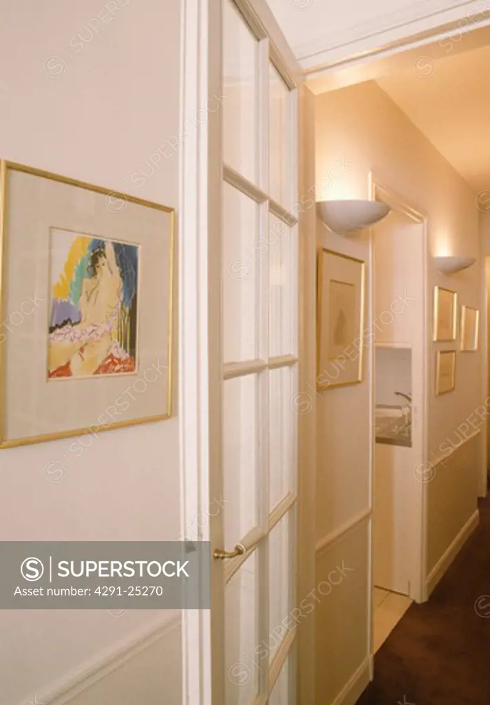 Picture beside glazed door in narrow white hall with uplighting