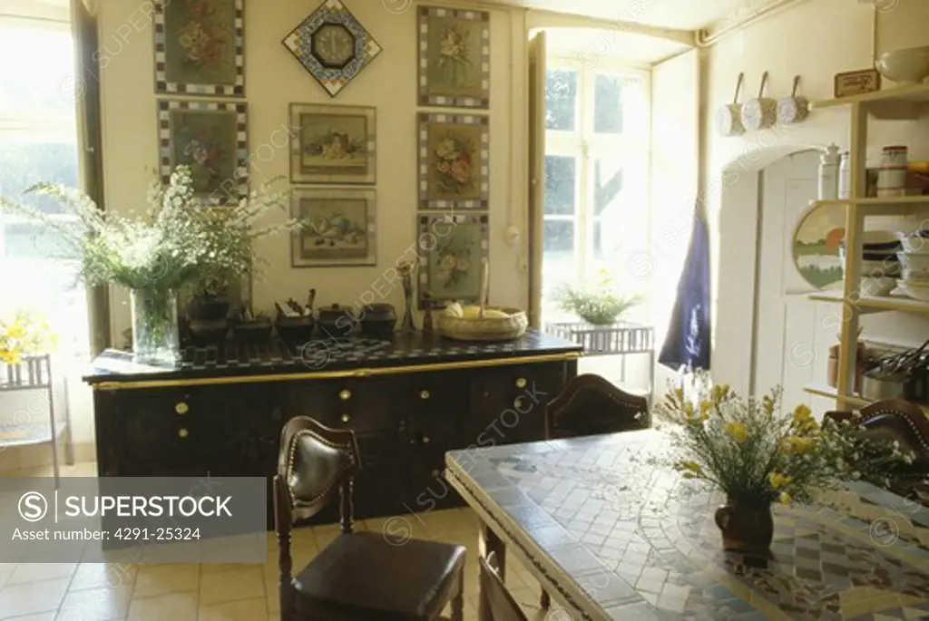 Mosaic-topped table and large black sideboard below group of pictures in French dining room
