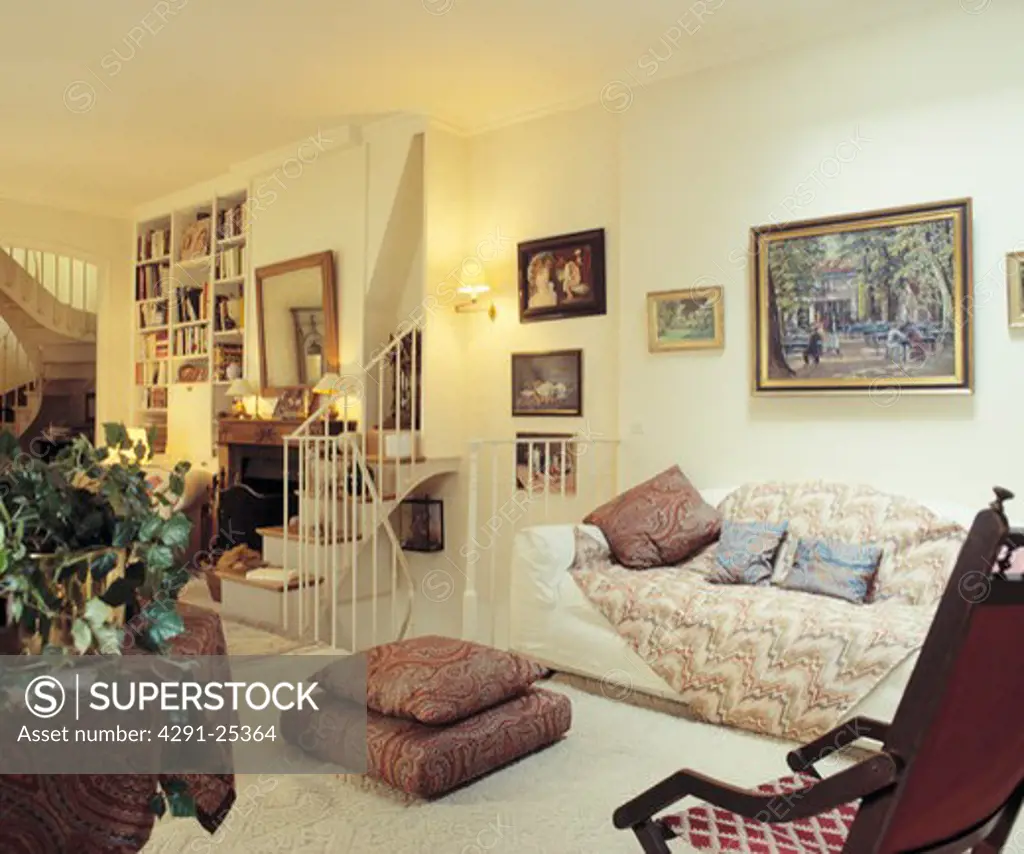 Collection of pictures above white sofa with quilted throw in living room with Paisley floor cushions and cream carpet
