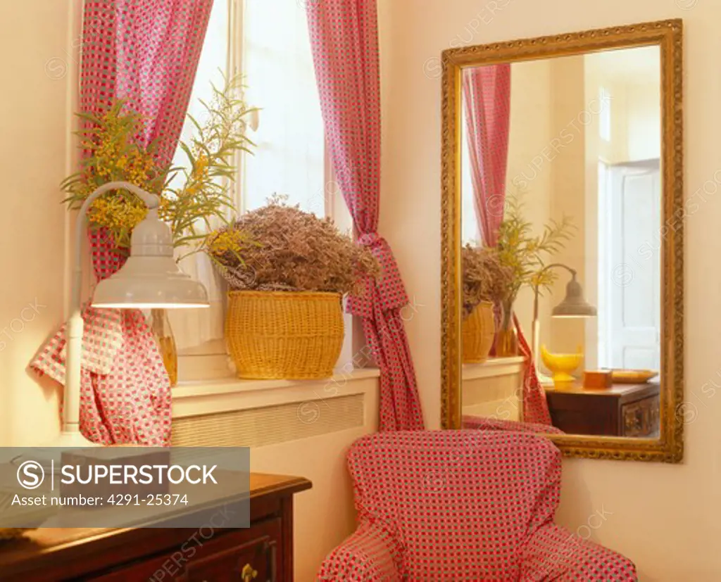 Pink armchair below mirror and window with pink curtains
