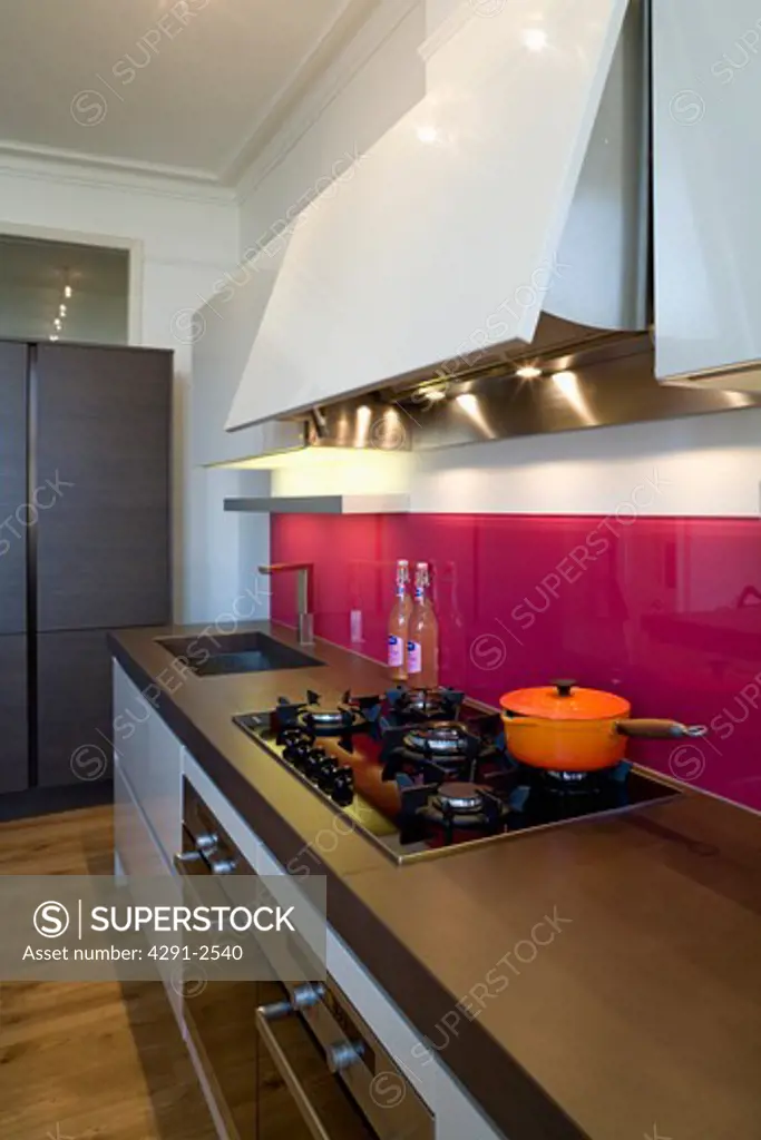 Orange pan on hob in modern kitchen with red glass splashbacks and cast concrete resin worktop