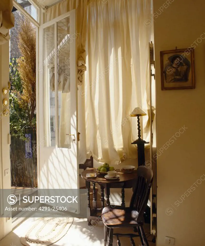 Old wooden chair and table in front of cream curtain in hall with open door