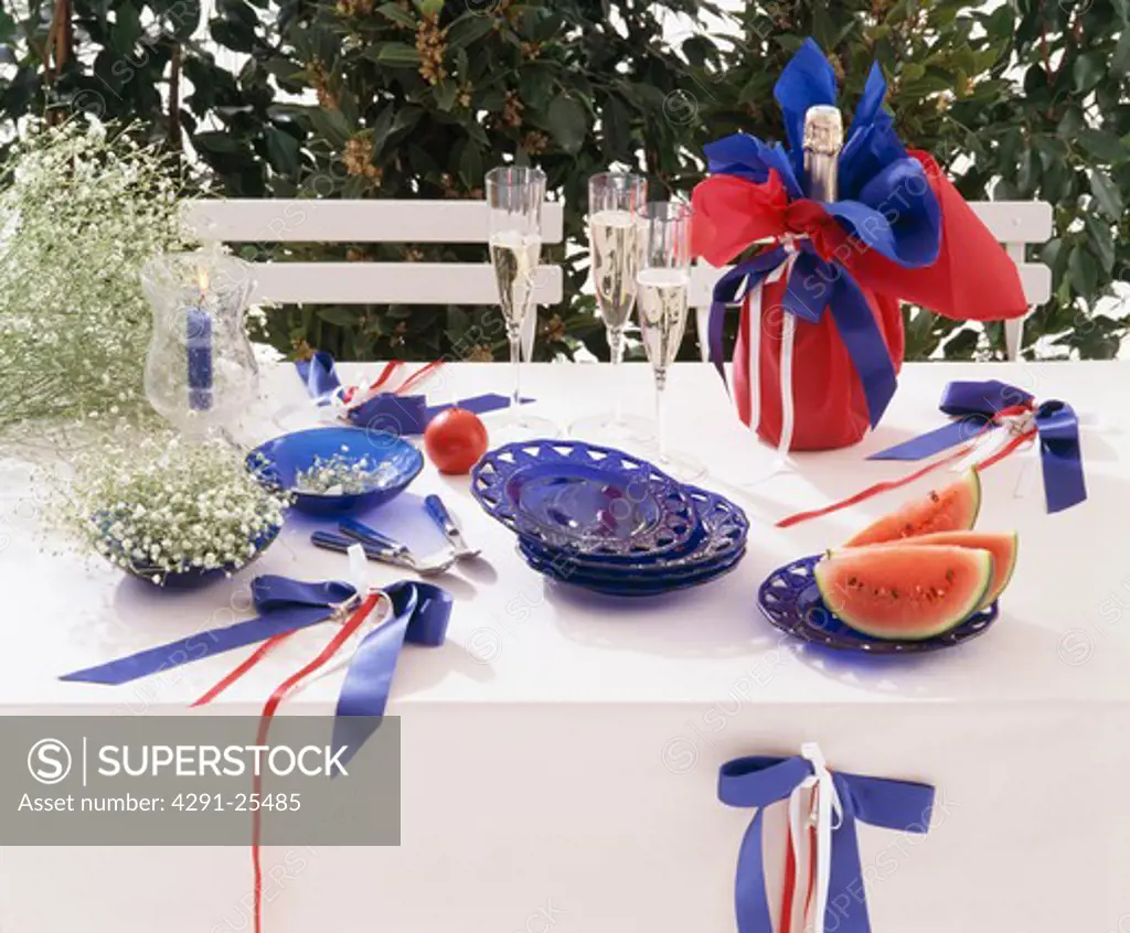 Close-up of table decorated for Bastille DAy with red, white and blue ribbons and bottle of champagne in red paper