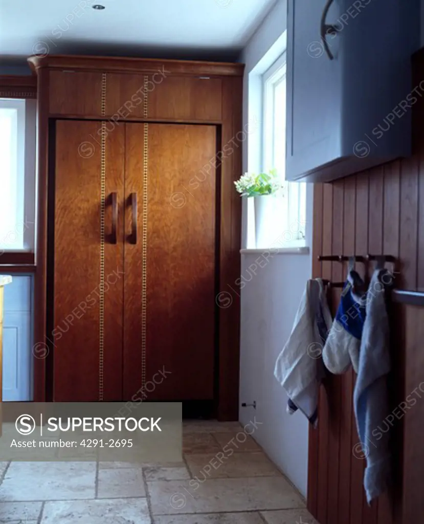 Large fridge-freezer concealed behind inlaid walnut doors in modern kitchen with travertine floor tiles