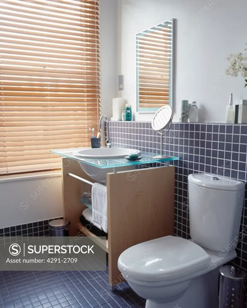 Basin in wooden vanity unit beside window with slatted blind in modern bathroom