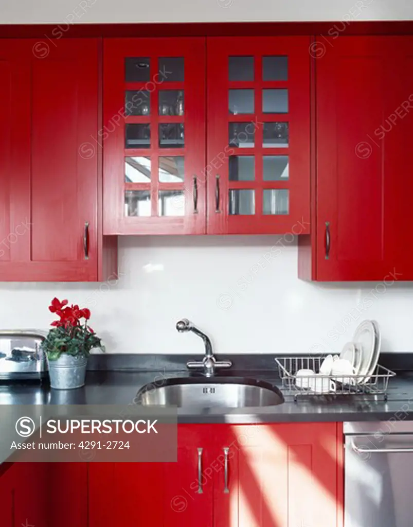 Close-up of red fitted wall cupboard above underset sink in black granite worktop