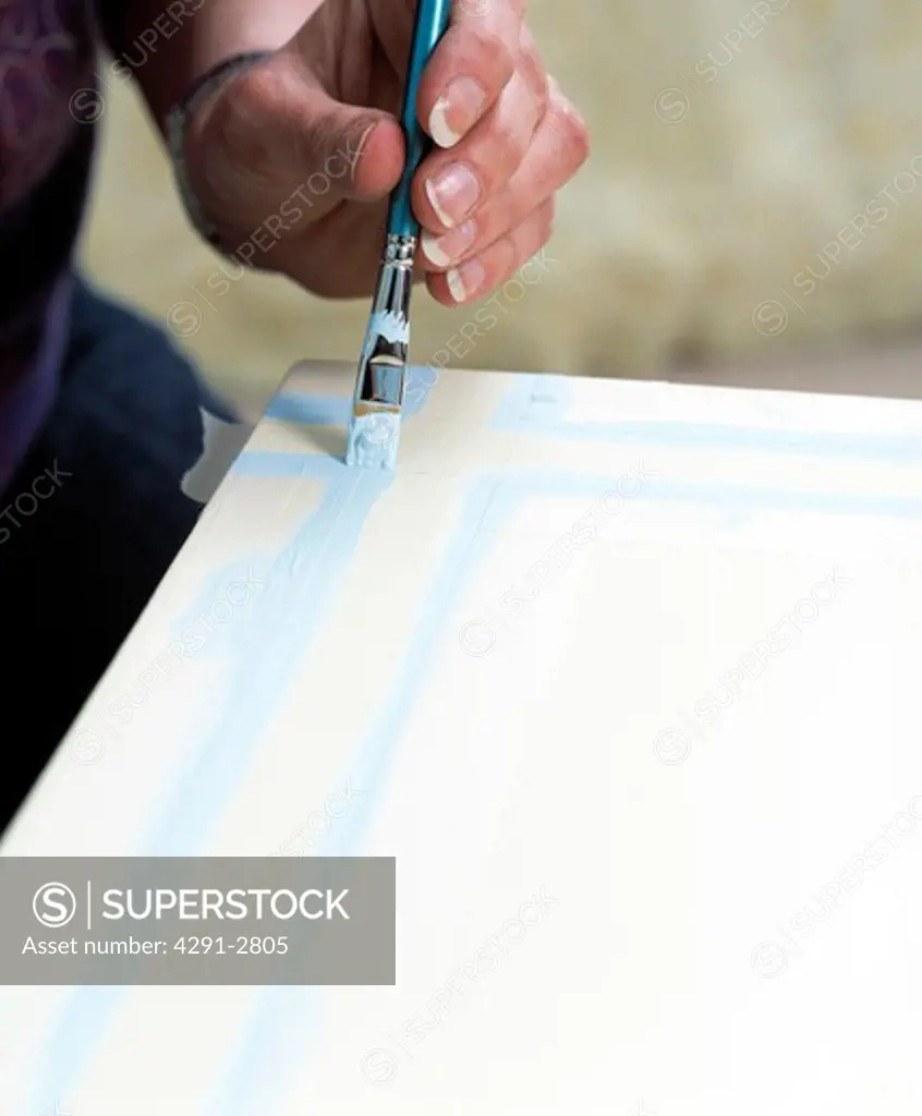 Close-up of hands painting blue line on table top