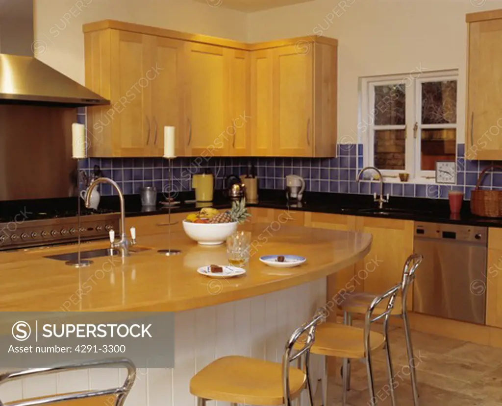 Chrome and wood stools at breakfast bar with wood worktop in modern kitchen with fitted wooden cupboards