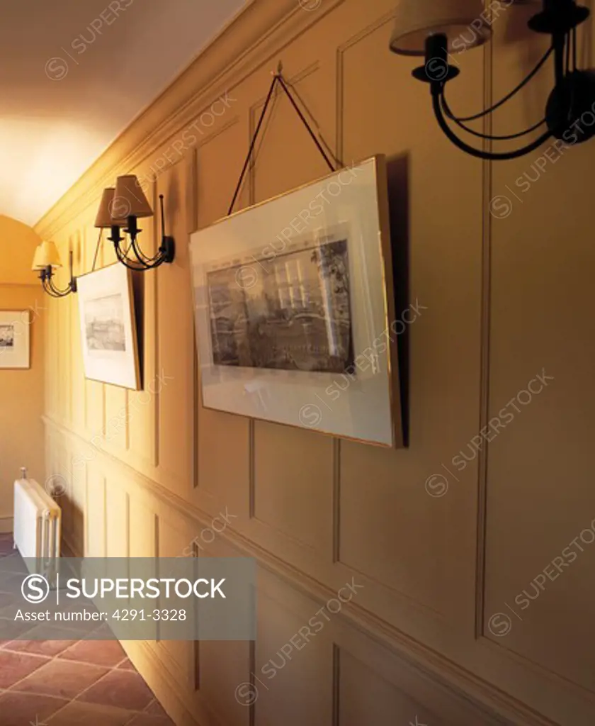 Pictures and wall-lights on cream panelled wall in country hall