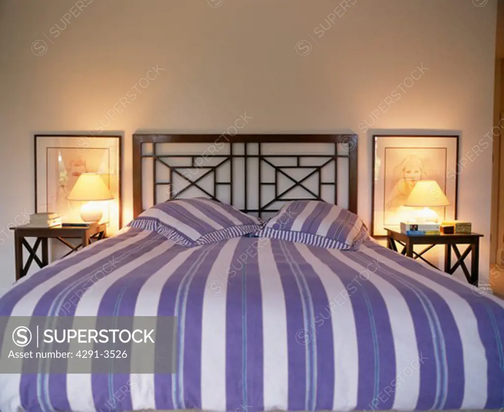 Blue and white striped bedlien on metal bed between lighted lamps on bedside tables