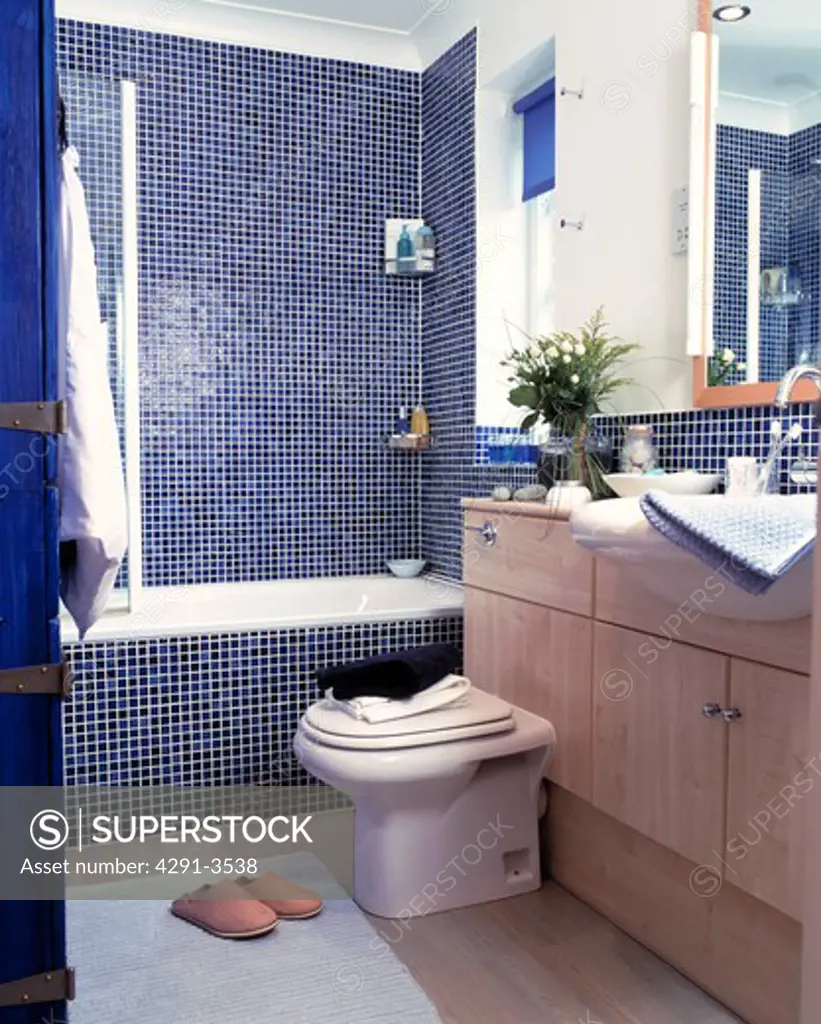 Blue mosaic tiles surround the bath and shower in this modern bathroom