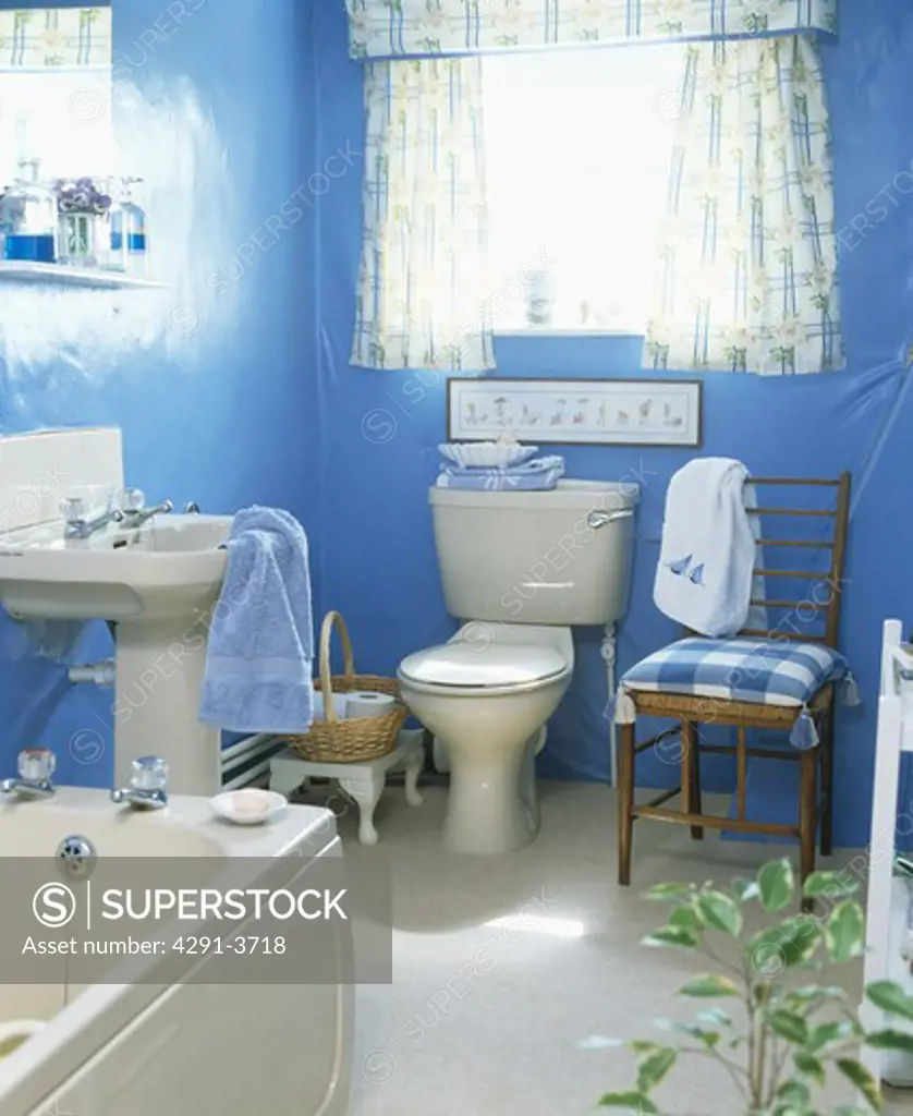 Blue checked chair beside toilet in small blue bathroom with white pedestal basin