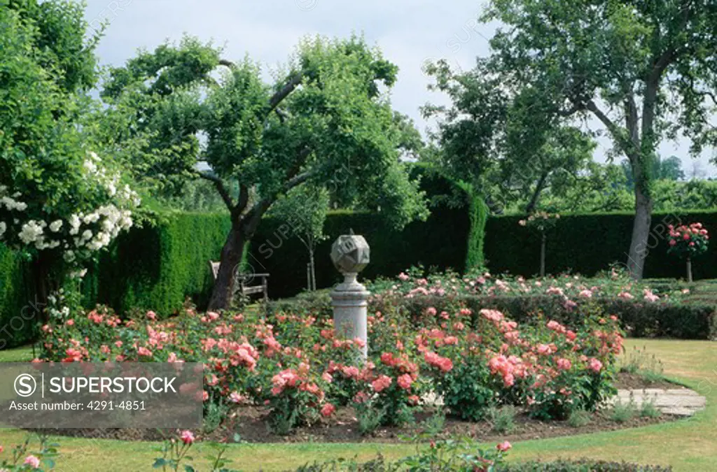 Sundial on plinth in circular bed with pink roses in large country garden