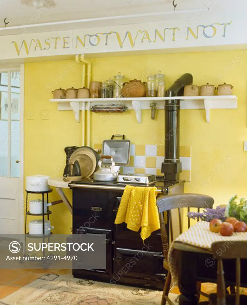 Stencilled graffiti text above terracotta pots and black Aga in traditional yellow kitchen with pans on freestanding rack