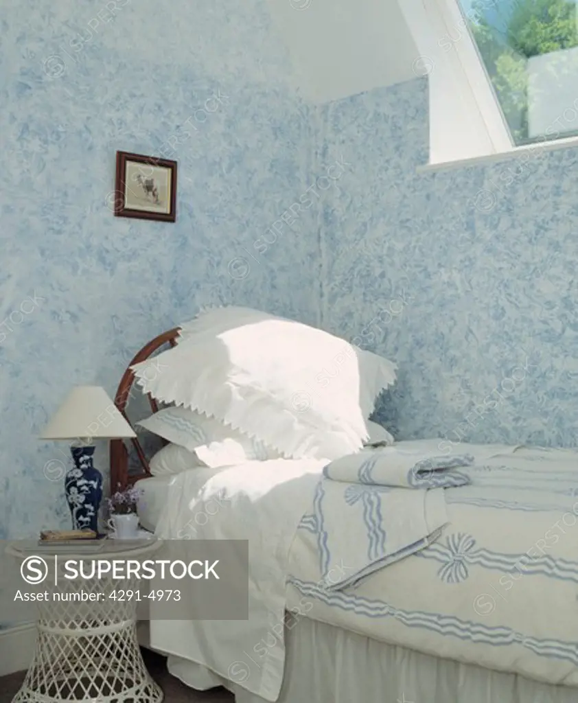 White pillows and blue and white duvet on bed below window in bedroom with painted stippled blue and white walls
