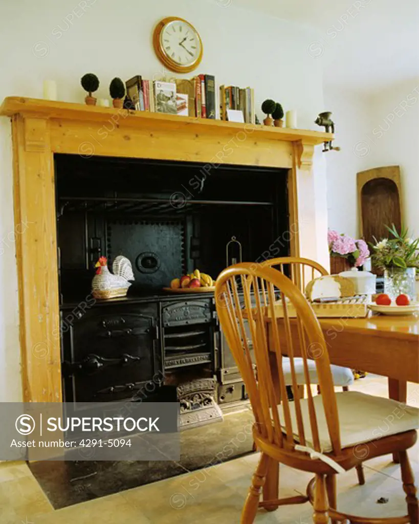 Pine mantelpiece with old black range stove in country dining room with Windsor chairs