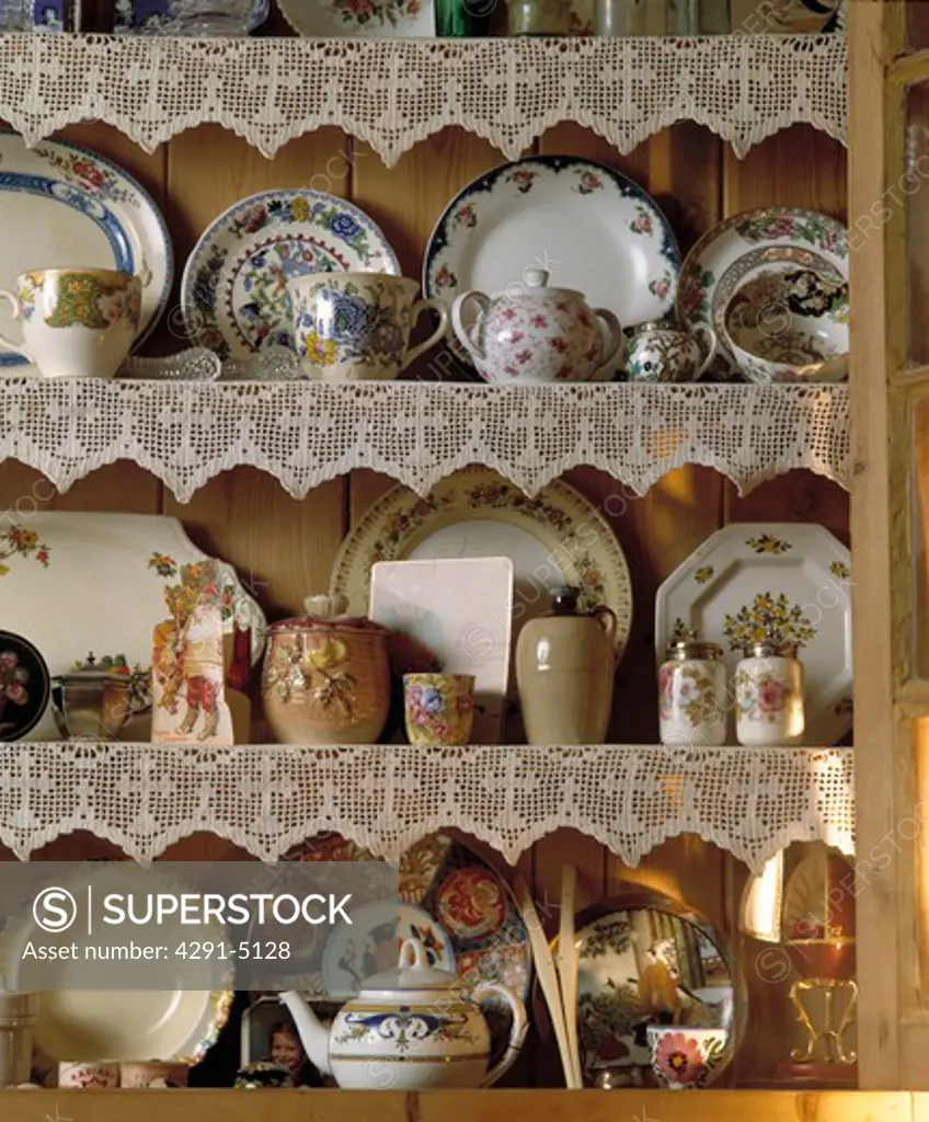 Close up of antique china plates and teapots on pine shelves with lace edging