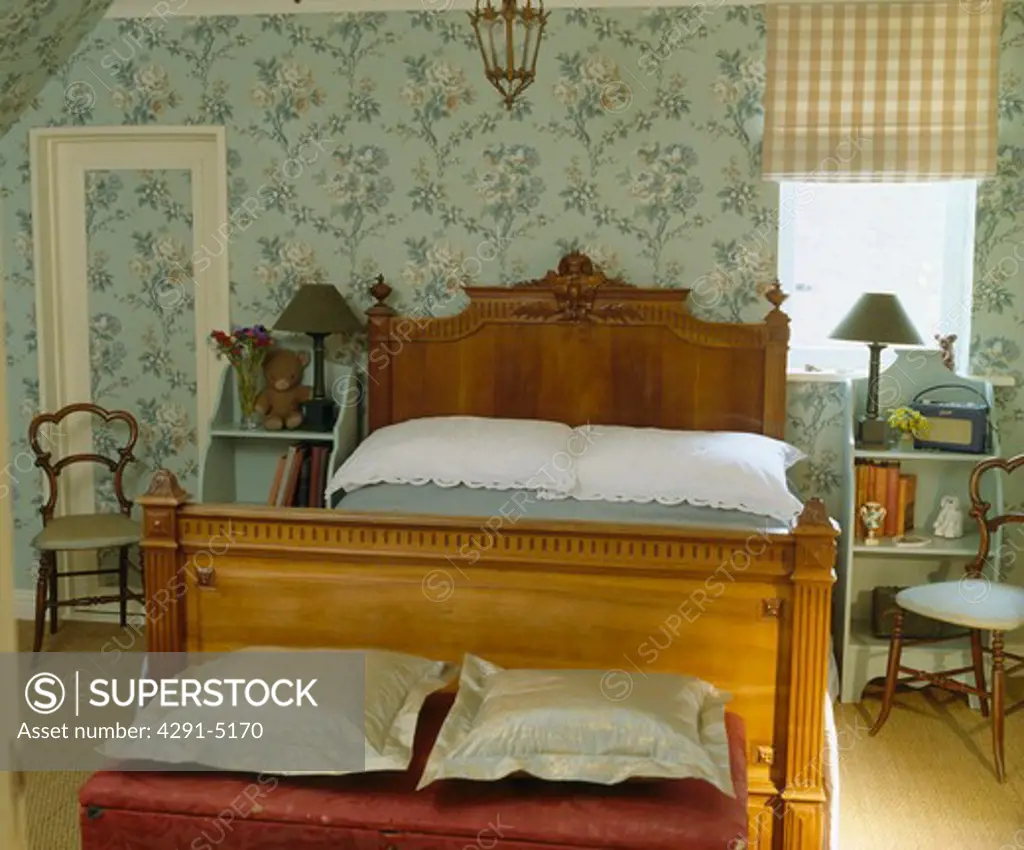 Antique wooden bed in country bedroom with blue floral wallpaper