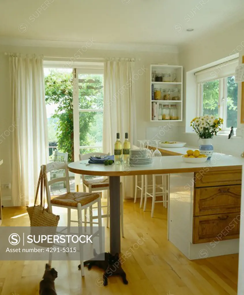 Rush-seated stool at breakfast bar in white country kitchen with French windows and wooden flooring