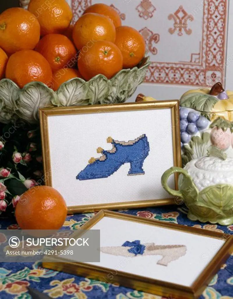 Close-up of bowl or oranges and gilt-framed cross-stitch picture of blue shoe