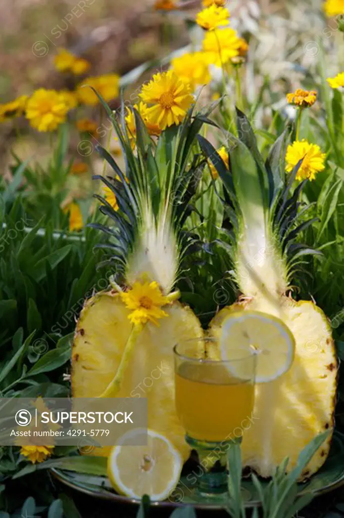 Close-up of halves of fresh pineapple with a glass of pineapple juice against background of yellow flowers