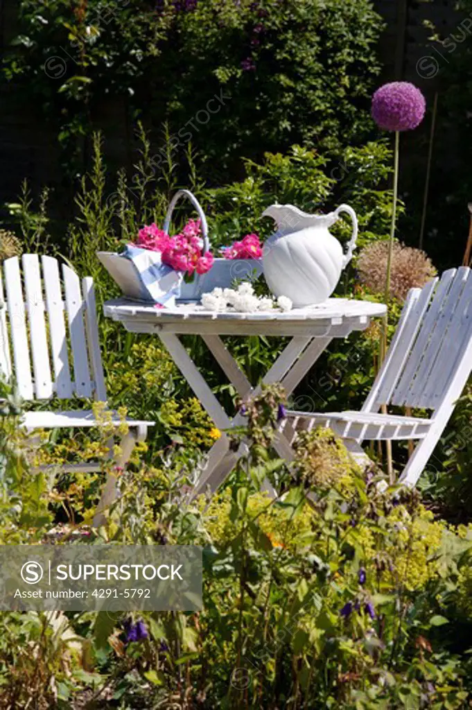 White chairs and table with white jug in country garden in summer
