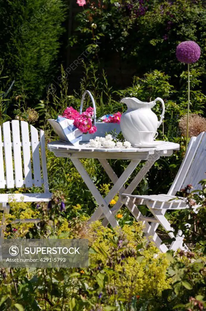 White chairs and table with white jug in country garden in summer