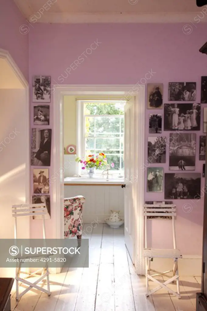 Black and white photographs on wall of pink landing with white chairs and floorboards and door open to bathroom