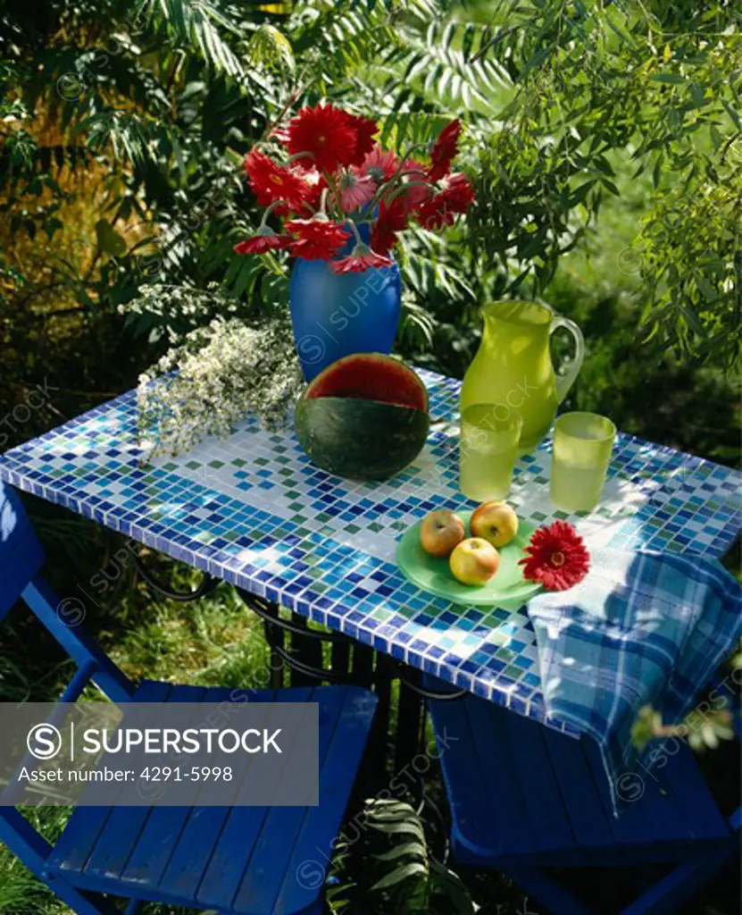 Close-up of lime-green glass jug and glasses on hand-made blue and white mosaic tile topped garden table with blue chair