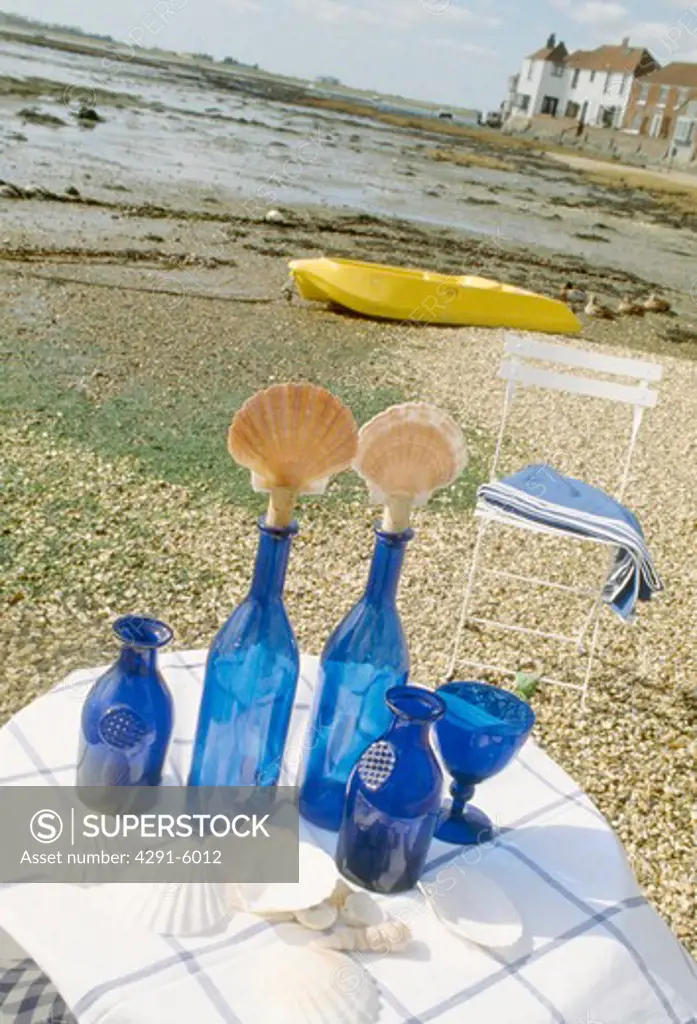 Blue glass bottles with seashell-stoppers on table on pebbled beach