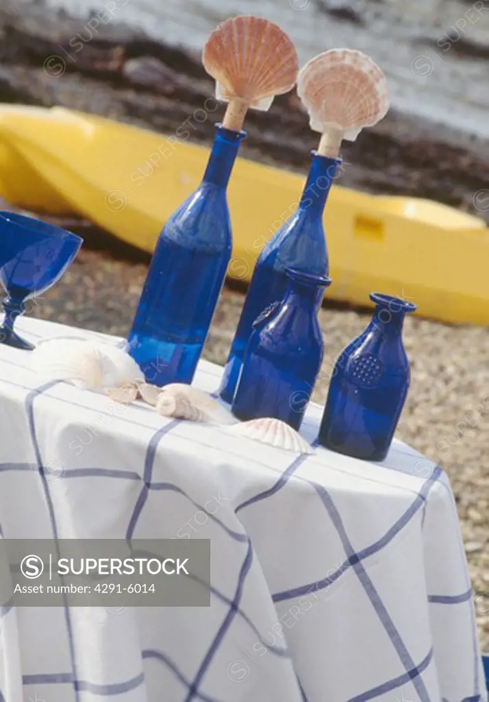 Close-up of blue bottles with seashell stoppers on table with checked cloth on beach