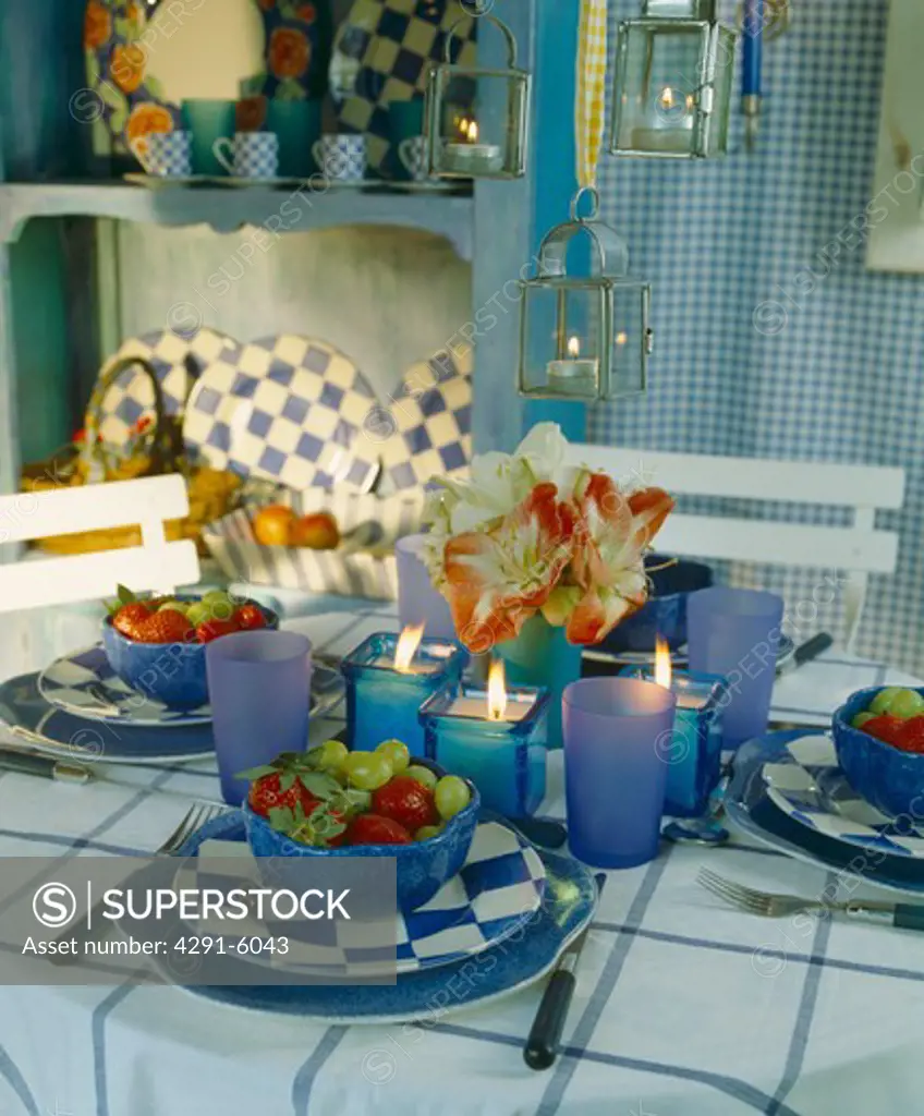 table with blue glass and blue and white checked crockery on table with candles in lanterns and blue holders
