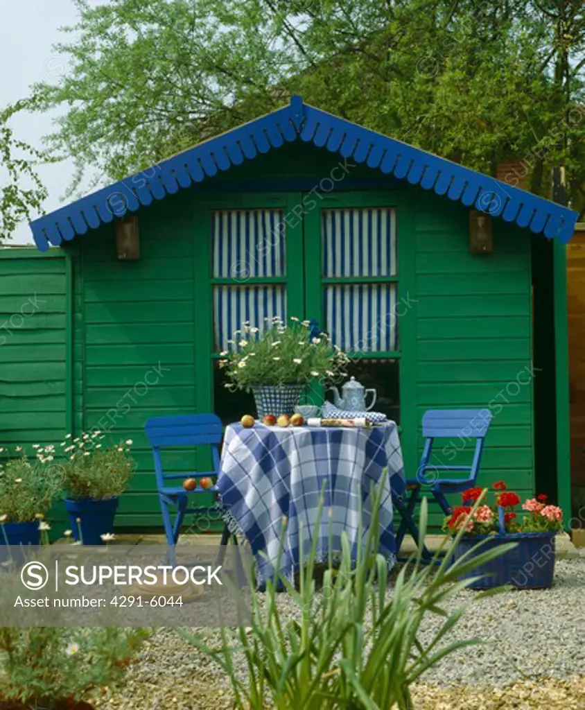 Blue chairs and table with checked cloth in front of blue and green painted wooden garden shed
