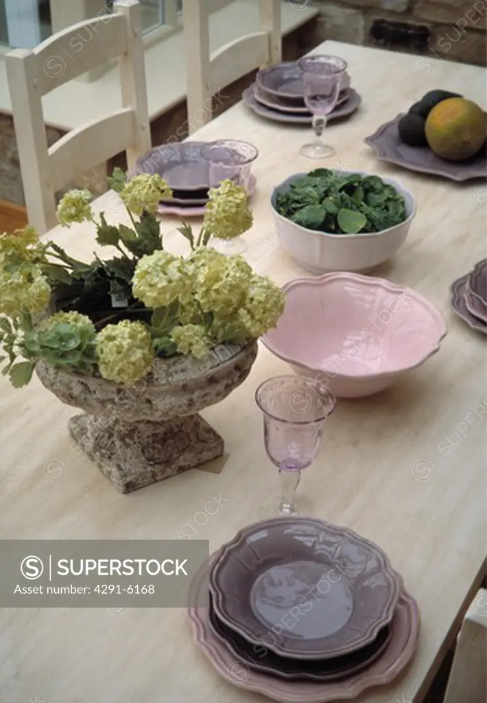 Close-up of mauve and pink crockery on limed wood table with green hydrangeas in stone vase