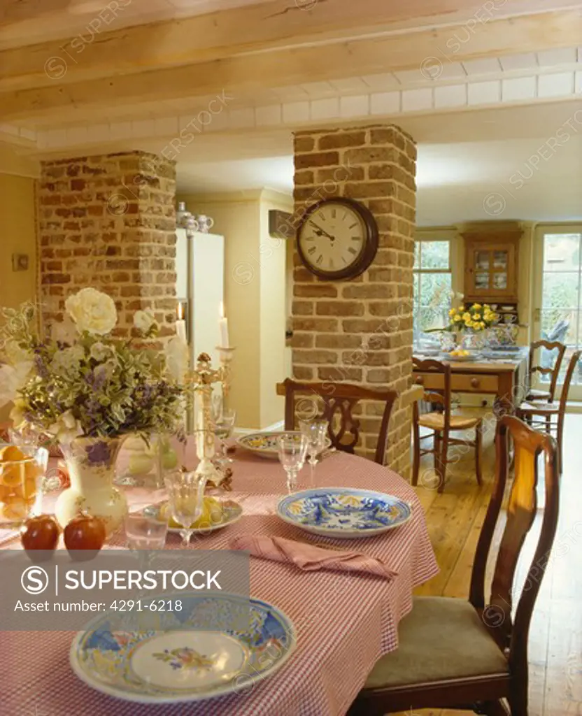 Circular antique clock on brick support wall in country dining room extension with pink cloth and place settings on table