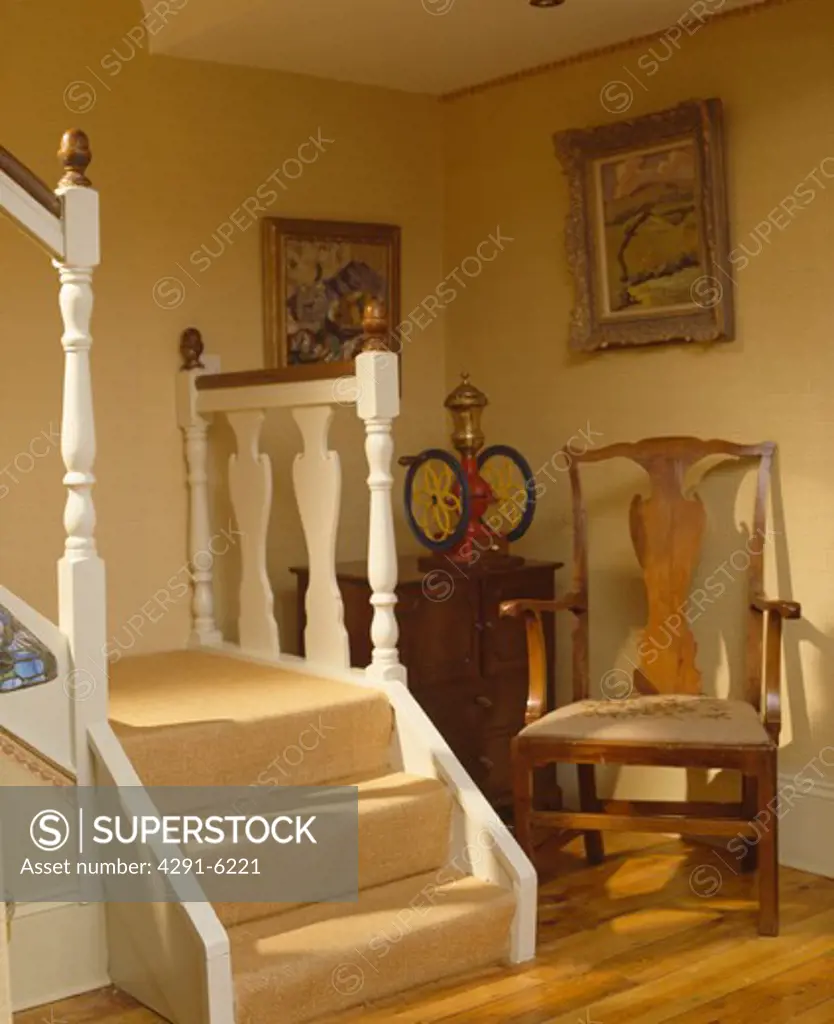 Antique chair in corner of neutral hall with cream carpet on the stairs