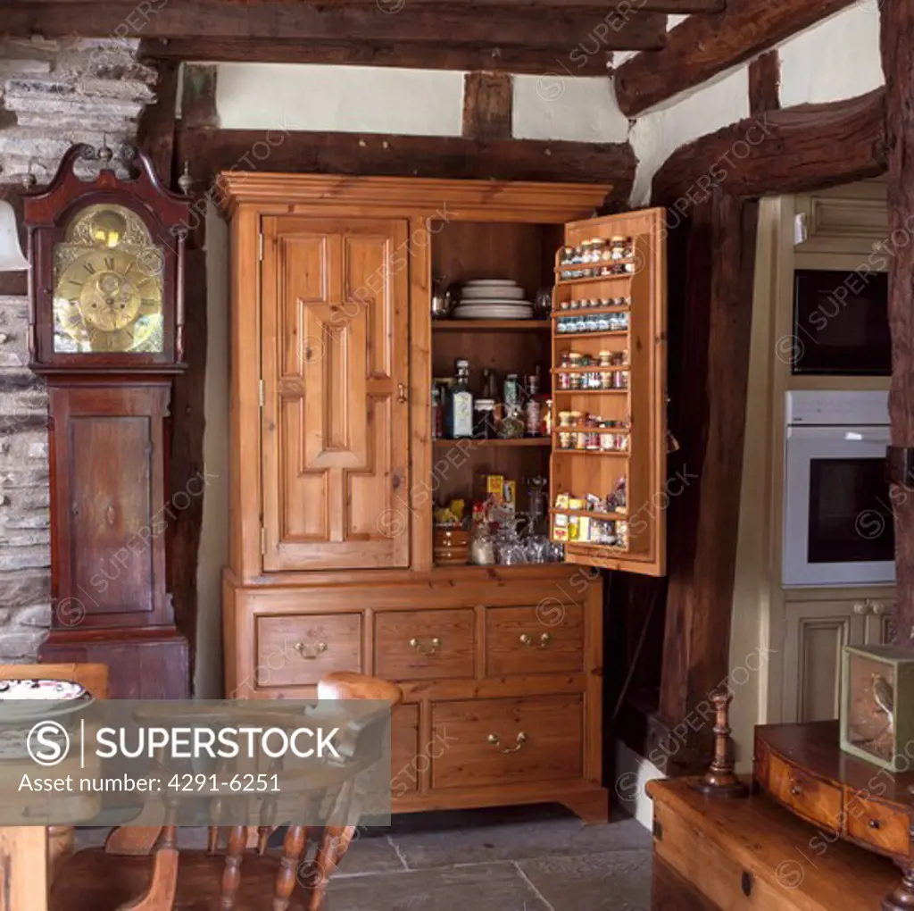Cottage kitchen with longcase clock beside large carved antique storage cupboard with door open