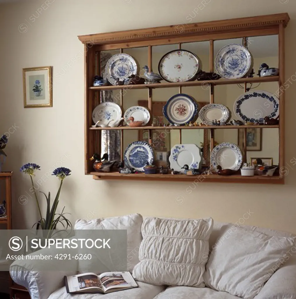 China plates on pine shelves over internal window above white sofa in living room