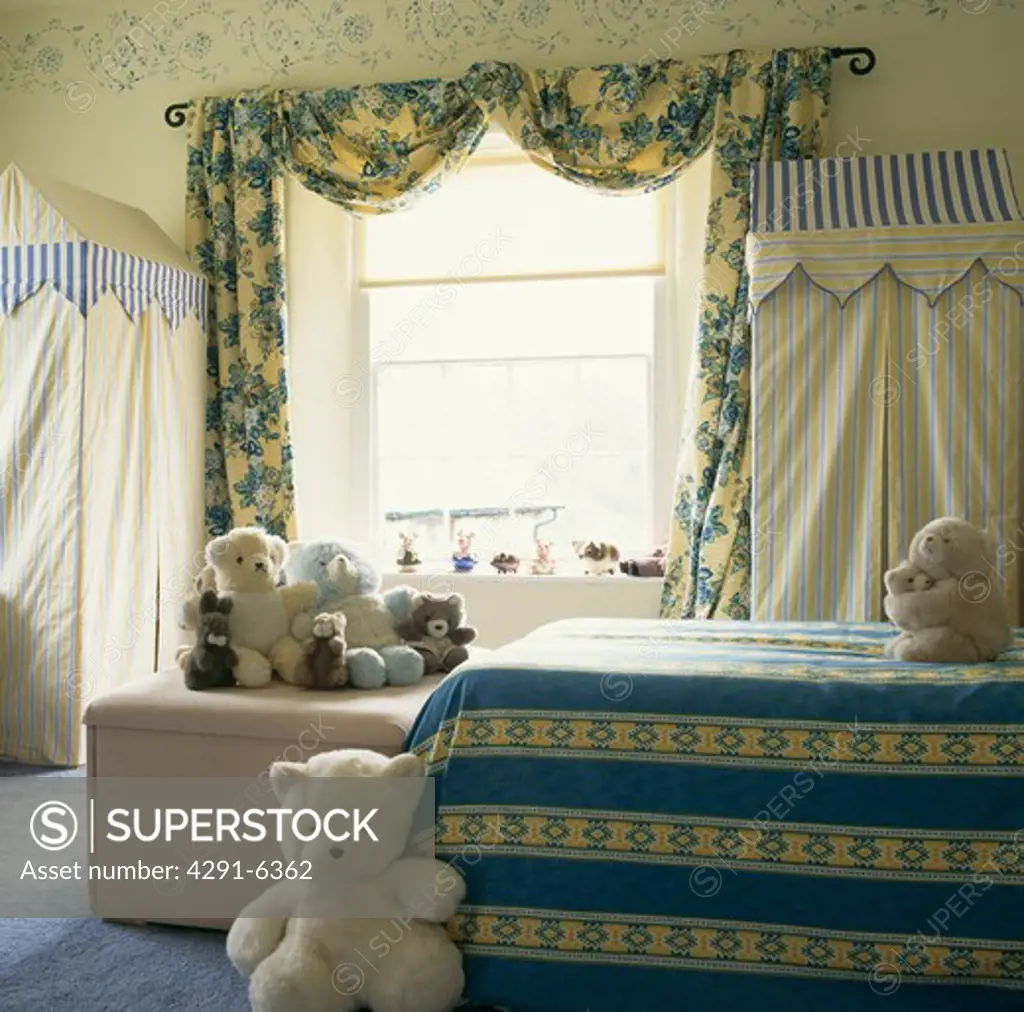 Blue and yellow floral curtains and striped bed linen in child's bedroom with teddy bears & striped fabric cupboards